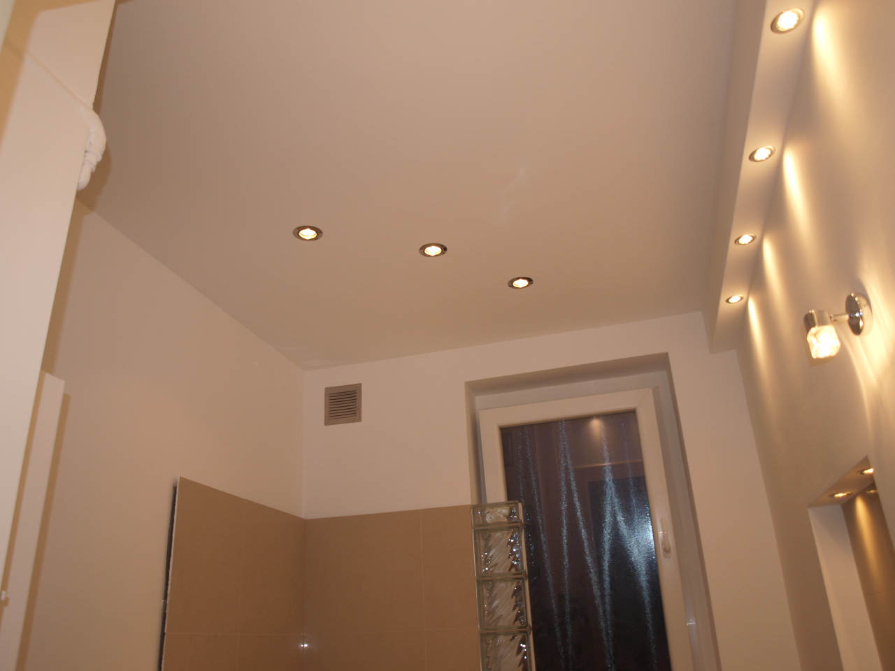 Wnętrze łazienki w trakcie prac, widoczne płyty G-K, sufit z oświetleniem punktowym, okno z luksferami i wentylacja.