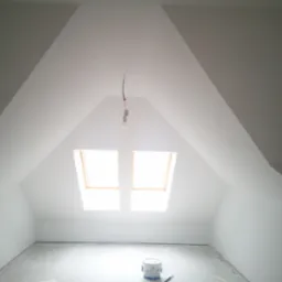 Poddasze po malowaniu na biało, z dwoma oknami dachowymi i wiszącą żarówką, na podłodze stoi puszka z farbą.