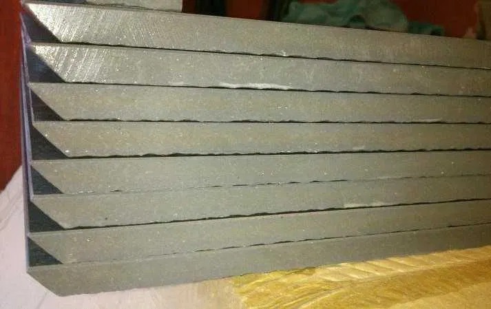 Stos szarych płytek, prawdopodobnie gresowych, ułożonych warstwami na sobie. Widoczne krawędzie z resztkami zaprawy.