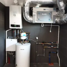 Kompletna instalacja grzewcza i wentylacyjna w kotłowni, widoczny kocioł grzewczy Buderus, rekuperator Pro-Vent Mistral Smart 400 z izolowanymi przewodami wentylacyjnymi, zbiornik na wodę...