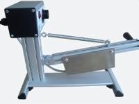 Niewielkie urządzenie przemysłowe w jasnej obudowie z elementami stalowymi, wyposażone w ostrze i mechanizm sprężynowy, widoczne przewody elektryczne.