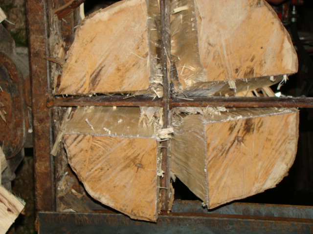 Rozłupane na cztery części drewno kominkowe w metalowej ramie, widoczne świeże wióry i pęknięcia.