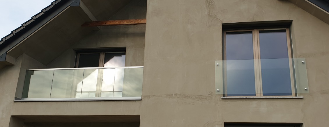 Szklana balustrada balkonowa zamontowana na budynku w Wieliczce, widoczna z zewnątrz, z elementami mocującymi ze stali nierdzewnej.