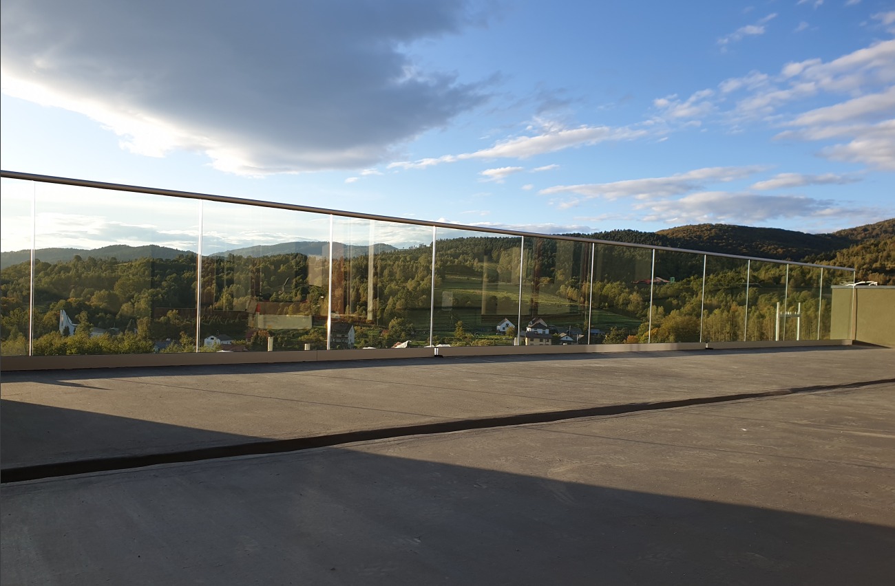 Szklana balustrada z metalową poręczą na tarasie z widokiem na górzysty krajobraz okolic Żywca, odbijający się w tafli szkła.