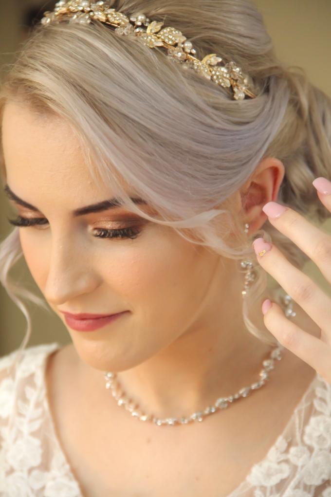 Portret panny młodej z delikatnym makijażem, złotą tiarą i naszyjnikiem, z bliska, z ręką uniesioną do twarzy i ozdobnym manicure.