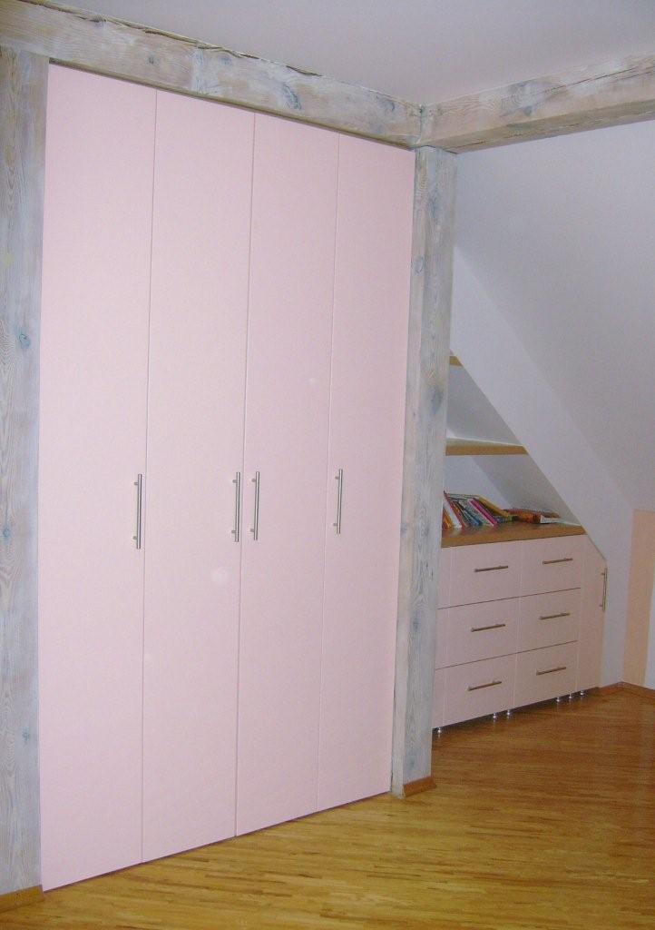 Różowa szafa z sześcioma drzwiami i srebrnymi uchwytami, zabudowana w pokoju na poddaszu, drewniane belki konstrukcyjne o bielonej powierzchni, obok zabudowa z szufladami pod skosem dachu.