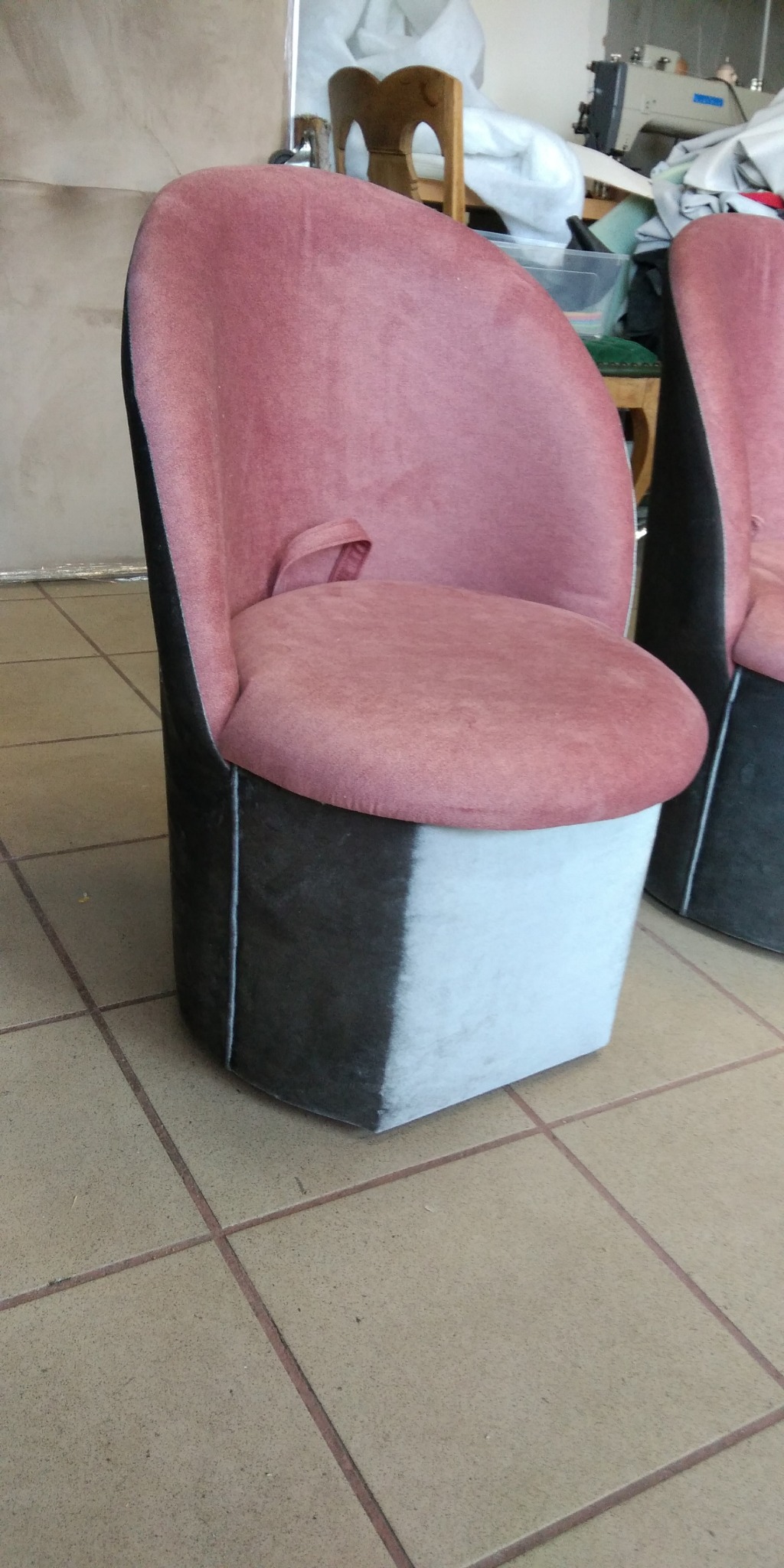 Różowe krzesło tapicerowane z czarno-białym dołem, widoczne drugie krzesło w tle, na podłodze z płytek.