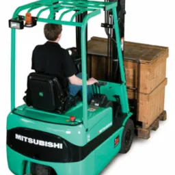 Elektryczny wózek widłowy MITSUBISHI SERIA FB10-15KRT PAC w trakcie podnoszenia drewnianych skrzyń, operator w kabinie, widoczny sygnał ostrzegawczy.