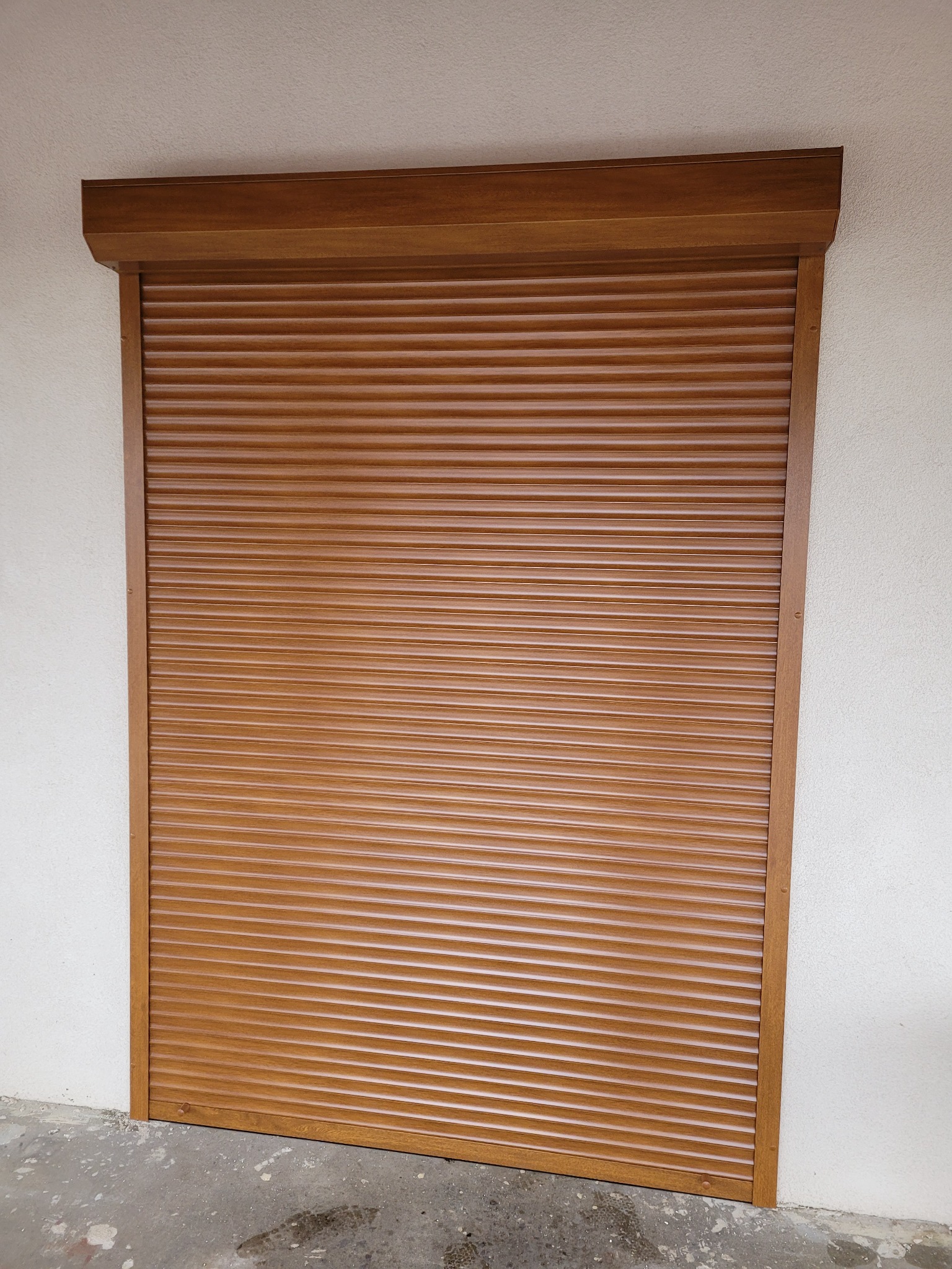 Zamknięta brązowa roleta zewnętrzna z lamelami, zamontowana na elewacji budynku, widoczna od frontu, z detalami mocowania.