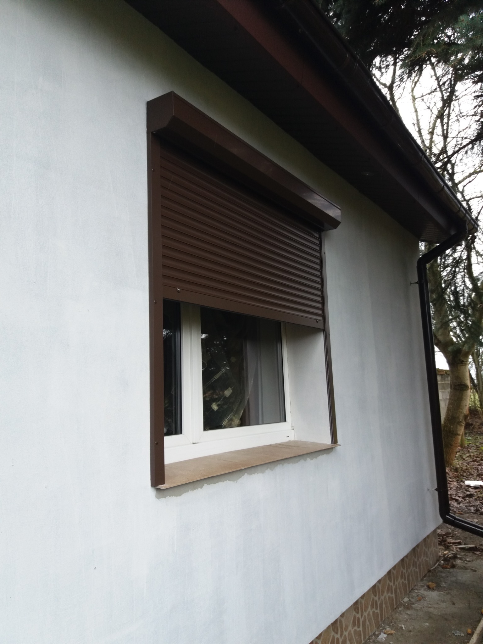 Brązowa roleta zewnętrzna zamontowana na oknie budynku w Gnieźnie, widok z boku na białą elewację i brązowe obramowanie okna.