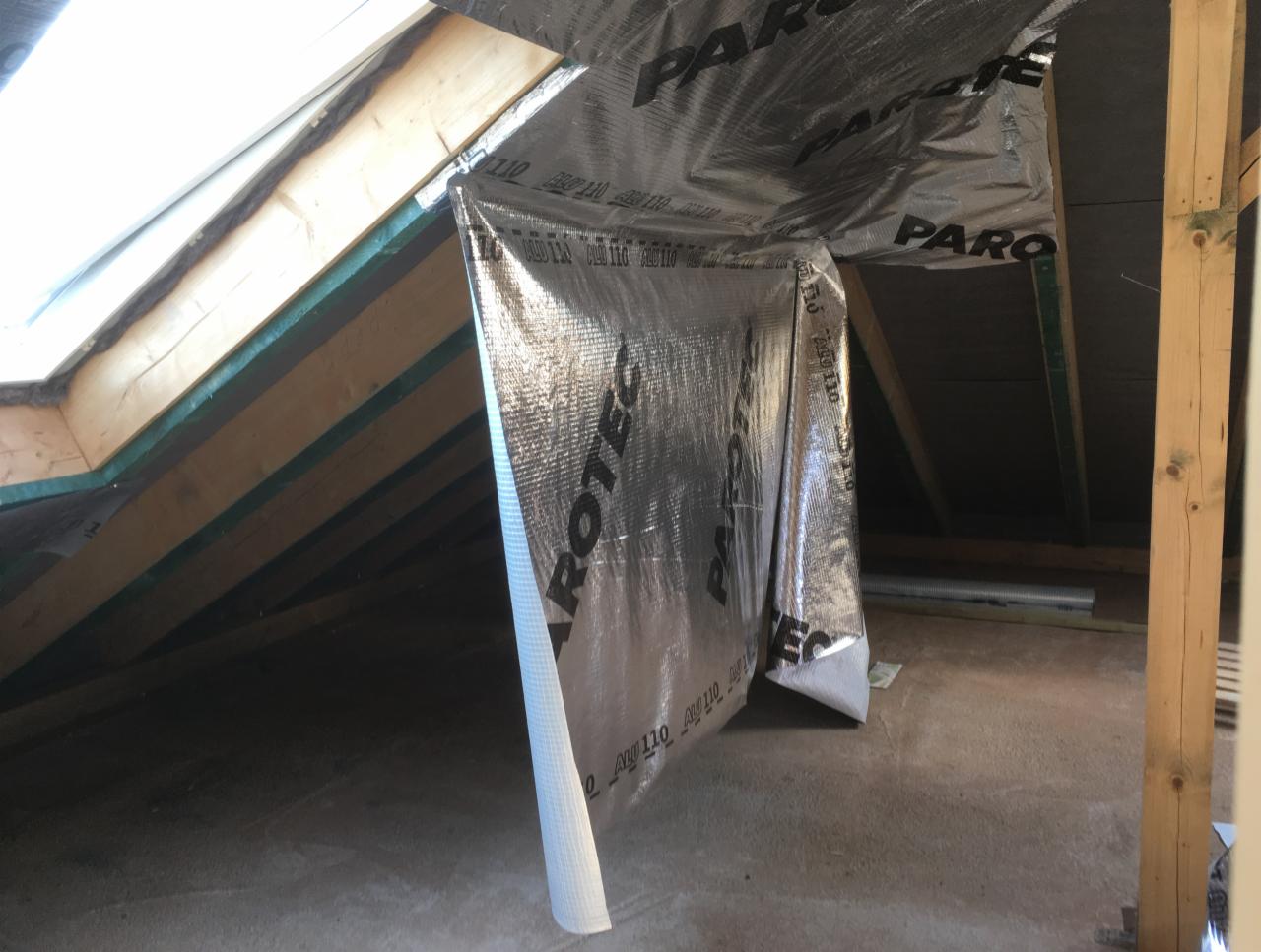 Folia paroizolacyjna z nadrukiem, zamontowana na drewnianej konstrukcji poddasza, widok na okno dachowe i fragment podłogi betonowej.