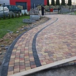 Max-bruk - Układanie kostki brukowej na podjeździe z widocznymi paletami kostki i przygotowanym podłożem, częściowo zakończona realizacja.