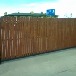 Przesuwna brama wjazdowa z drewnianymi sztachetami w Ząbkach, widoczny numer posesji '123' oraz znak drogowy w tle.