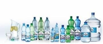 Szeroki kadr prezentujący różnorodne butelki wody mineralnej i dzbanek z wodą i cytryną, ustawione na białym tle, z widocznymi etykietami producenta.