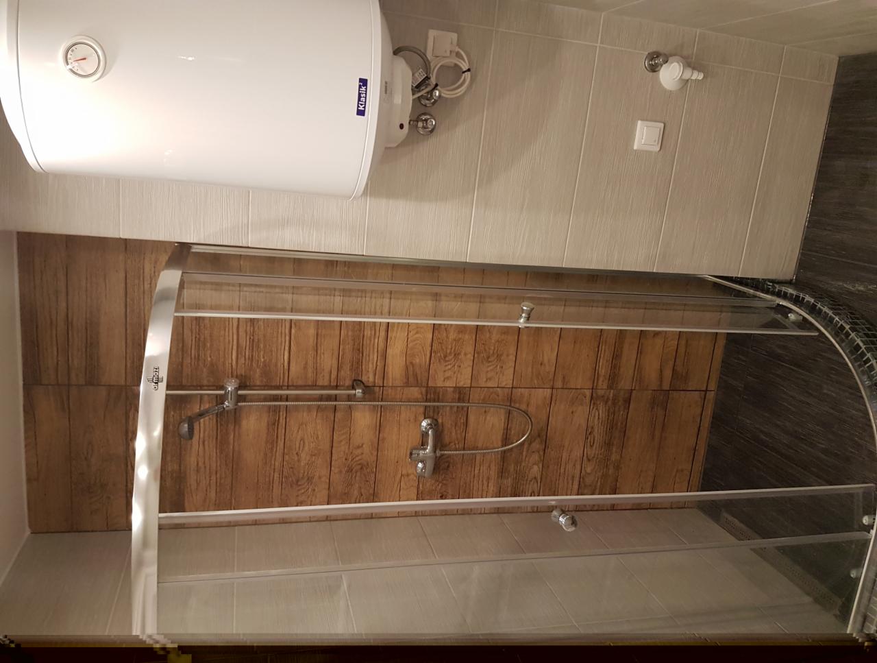 Nowoczesna kabina prysznicowa z drewnopodobną okładziną ścienną, widoczny bojler elektryczny 'Klasik' i jasne płytki ceramiczne na ścianie, chromowana armatura.