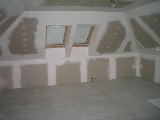 Poddasze w trakcie przygotowania do malowania: płyty gipsowo-kartonowe z widocznymi łączeniami, częściowo pokryte masą szpachlową, surowy beton na podłodze, dwa okna dachowe.