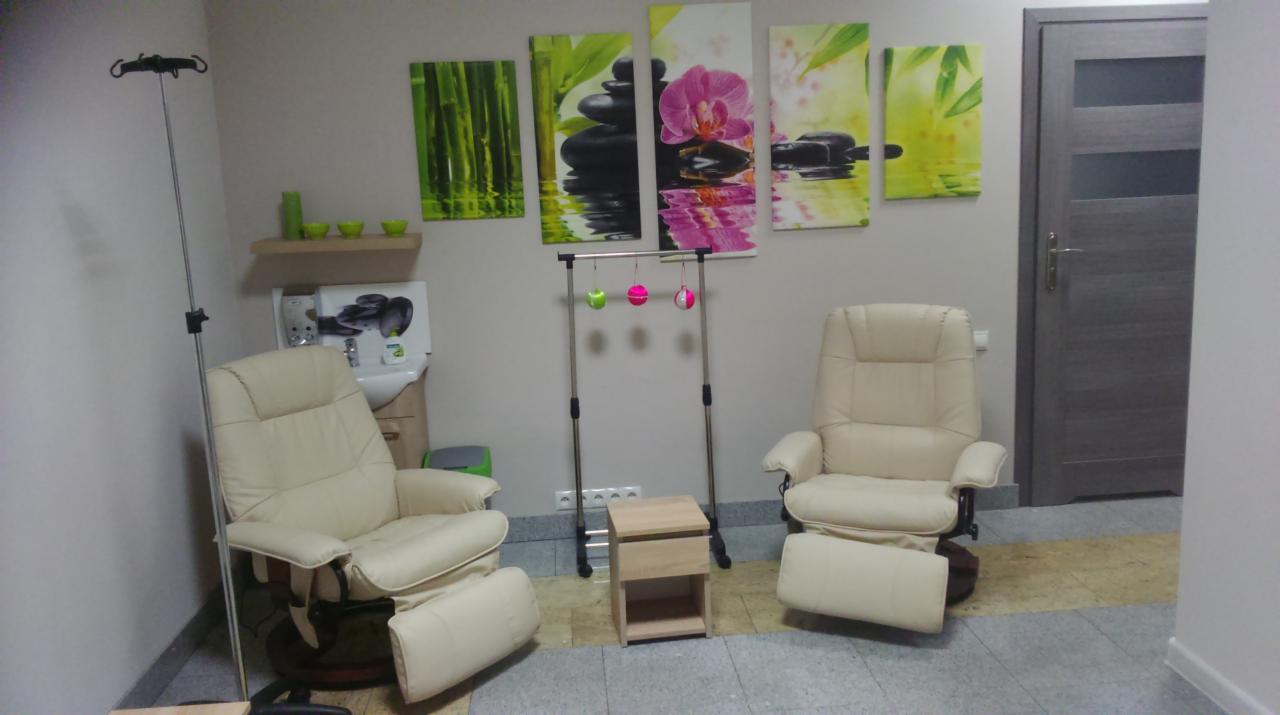 Jasne, skórzane fotele relaksacyjne w gabinecie z elementami dekoracyjnymi w stylu zen: obrazy z motywem bambusa, kamieni i orchidei, oraz lampa do kroplówek po lewej stronie.