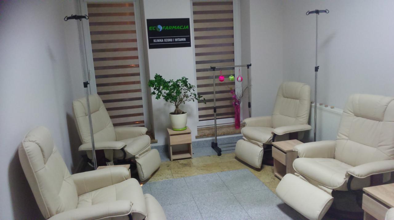 Wnętrze gabinetu z trzema beżowymi fotelami z regulowanym podnóżkiem, stojakami na kroplówki, rośliną doniczkową i logo 'EC Farmacja Klinika Ozonu i Witamin' na ścianie.