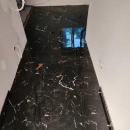 Ułożona, czarna, błyszcząca podłoga z marmurkowym wzorem w nowym wnętrzu, widoczne białe ściany z wystającymi przewodami elektrycznymi.