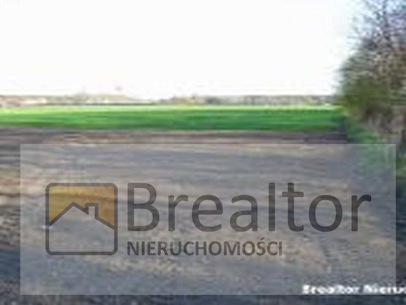 Działka budowlana z widocznym logo firmy Breator Nieruchomości, na pierwszym planie przygotowany grunt, w tle zieleń i drzewa.