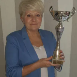 Uśmiechnięta kobieta w błękitnym żakiecie trzyma w dłoniach srebrny puchar z inskrypcją 'VIP Generali Sabina Króliczek'