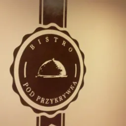 Brązowy logotyp 'Bistro Pod Przykrywką' z rysunkiem klosza na ścianie, widoczne fragmenty kremowego fotela.