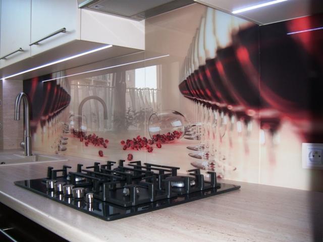 Szklany panel kuchenny z motywem kieliszków wina i rozrzuconych owoców, zamontowany nad płytą gazową. Uzupełniony oświetleniem LED podszafkowym.