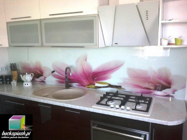 Szklana okładzina ścienna z motywem kwiatowym nad blatem kuchennym z zlewozmywakiem i płytą gazową w nowoczesnej kuchni z białymi szafkami.