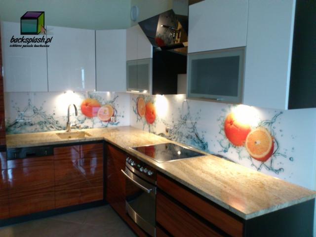 Kuchnia z panelami szklanymi z motywem owoców cytrusowych, oświetlona punktowo. Fronty szafek białe, blaty kamienne, a dolne szafki w odcieniach brązu.