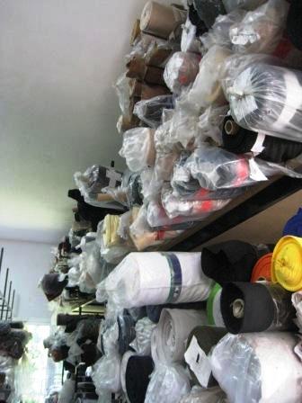 Magazyn z półkami wypełnionymi rolkami tkanin, każda zapakowana w przezroczystą folię, ukazując różne kolory i faktury materiałów.