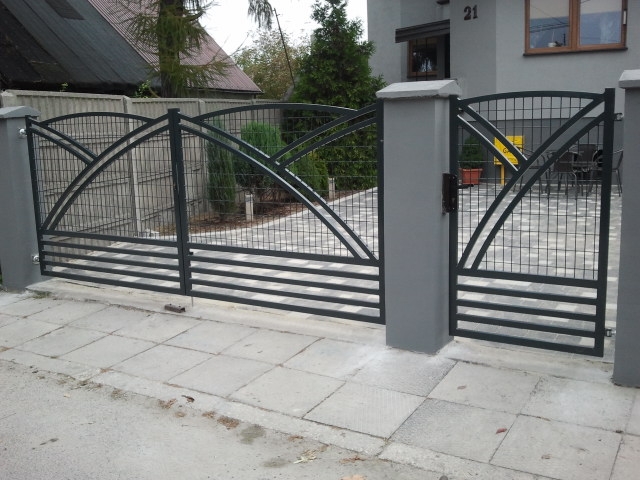 Nowoczesne ogrodzenie metalowe z bramą wjazdową, pomalowane na szaro, zlokalizowane przed domem w Kielcach, z widocznymi elementami dekoracyjnymi w górnej części.