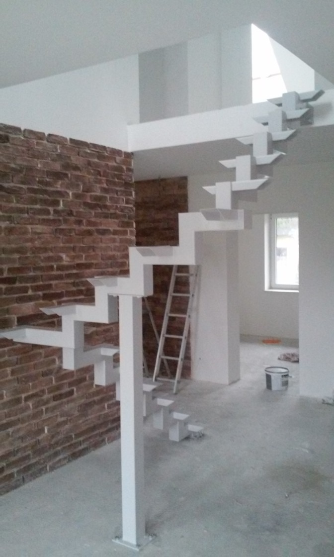 Nowoczesne, białe schody metalowe o geometrycznym kształcie, zamontowane w pomieszczeniu z ceglaną ścianą. Widoczna drabina oparta o ścianę i wiadro z farbą na podłodze.
