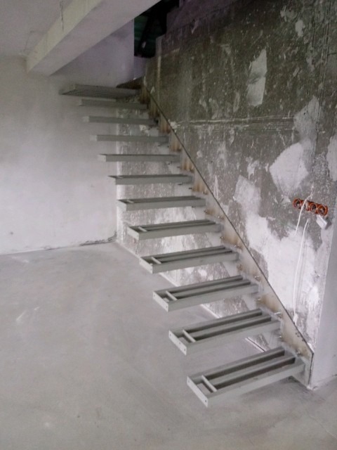 Konstrukcja schodów metalowych z profilami w surowym stanie, przed wykończeniem, na tle ściany w trakcie prac wykończeniowych.