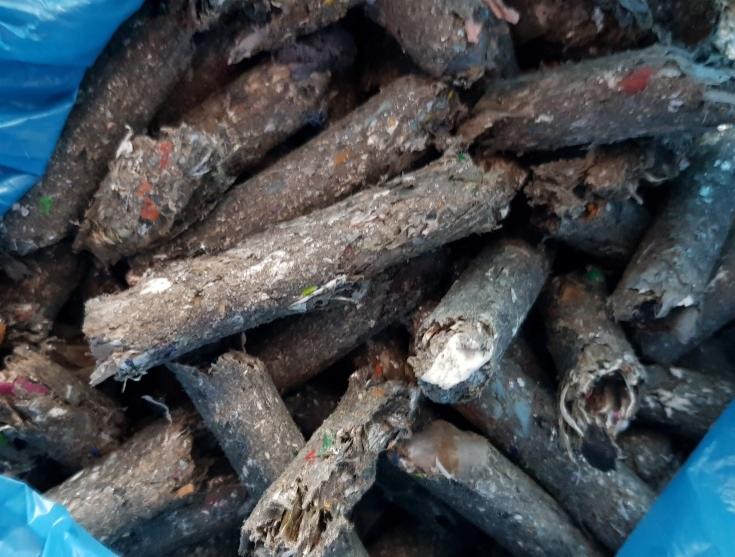 Stos zużytych, sprasowanych brykietów z odpadów w niebieskim worku foliowym, widoczne fragmenty plastiku i papieru.