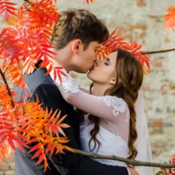 Pocałunek nowożeńców w Częstochowie, otulonych jesiennymi liśćmi na tle ceglanej ściany.