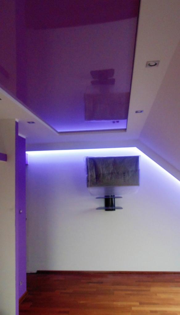 Fioletowy sufit napinany z połyskiem, oświetlenie LED wzdłuż krawędzi, drewniana podłoga. Nowoczesny design wnętrza poddasza.