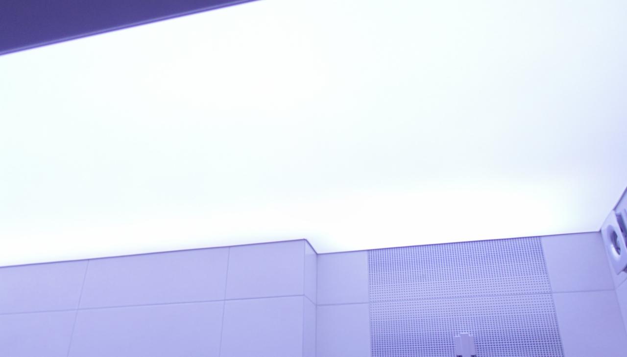 Biały sufit napinany z oświetleniem LED, widoczny fragment ściany z perforowanym panelem w odcieniach bieli i fioletu, nowoczesne wykończenie.