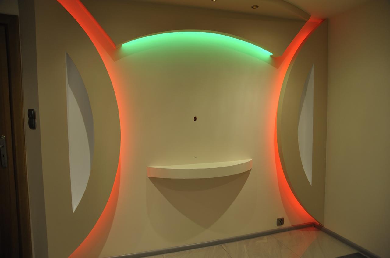 Nietypowa aranżacja ściany z podświetleniem LED: czerwone i zielone światło akcentują wnęki i półkę. Nowoczesny design wnętrza.