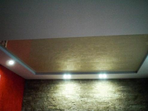 Wykończony sufit podwieszany z oświetleniem punktowym i dekoracyjną ścianą z kamienia. Widoczny fragment czerwonej ściany po lewej stronie.