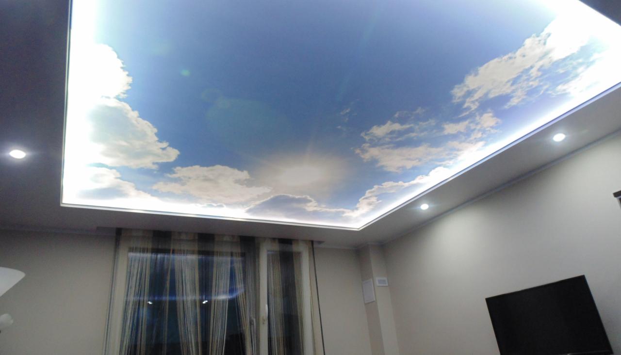 Sufit napinany z motywem nieba i chmur, podświetlany LED, widok z dołu na tle okna z zasłonami i telewizora.