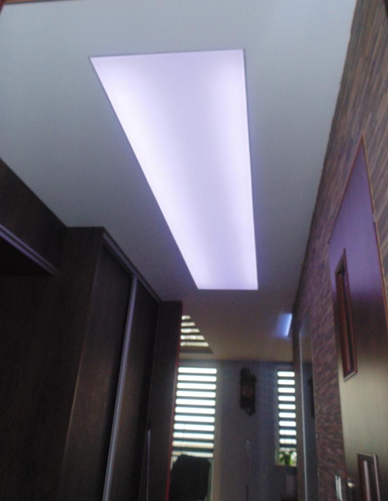 Podwieszany sufit z prostokątnym oświetleniem LED w nowoczesnym wnętrzu, widok z dołu, ciemne meble i żaluzje w tle.