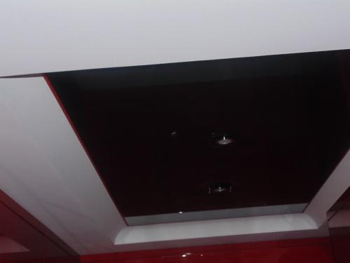 Czarne lustrzane odbicie w suficie podwieszanym z wbudowanymi punktowymi lampami, otoczone białym obramowaniem i czerwonymi ścianami.