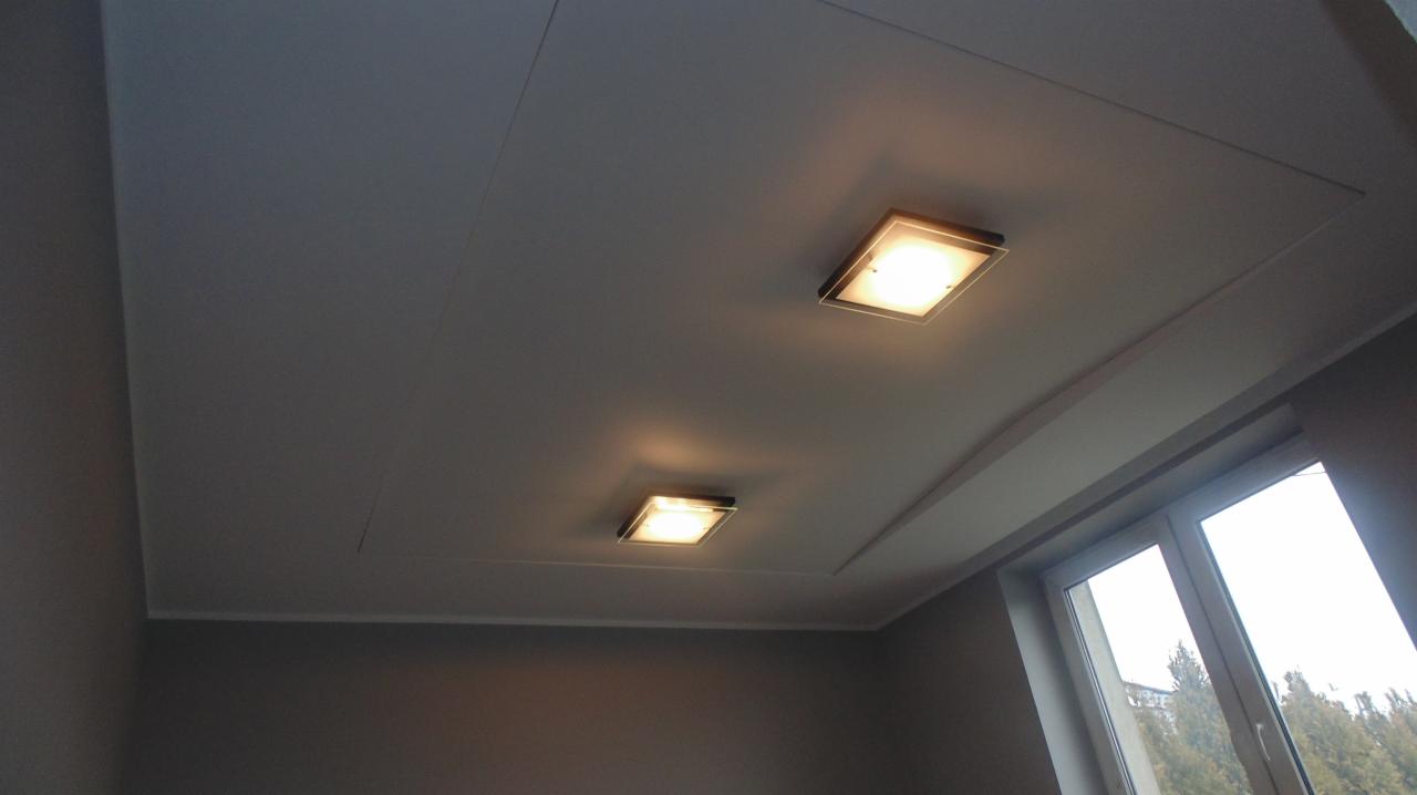 Szary sufit z dwoma kwadratowymi lampami wpuszczanymi, widok z dołu pod kątem, z oknem w tle. Wykończenie wnętrza.