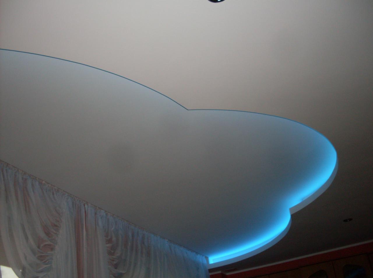 Biały sufit podwieszany z niebieskim podświetleniem LED, widok z dołu, fragment zasłony w lewym dolnym rogu.