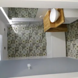 Nowoczesna łazienka z wzorzystymi płytkami na ścianach, białą umywalką nablatową na drewnianym blacie i szarą podłogą, oświetlenie LED w suficie.