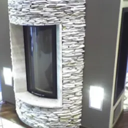 Nowoczesny kominek z obudową z kamienia naturalnego, półokrągły kształt, czarny wkład kominkowy, oświetlenie punktowe na ścianie.