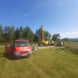 WITOLD STOPYRA FHU. WIT-WIERT - Czerwony samochód dostawczy firmy WIT-WIERT z otwartymi drzwiami na trawniku, w tle żółta wiertnica podczas pracy przy wierceniu studni w słoneczny dzień.