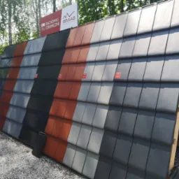 Ekspozycja ceramicznych pokryć dachowych w różnych kolorach, marki Braas, prezentowana na drewnianej konstrukcji na żwirowym podłożu.