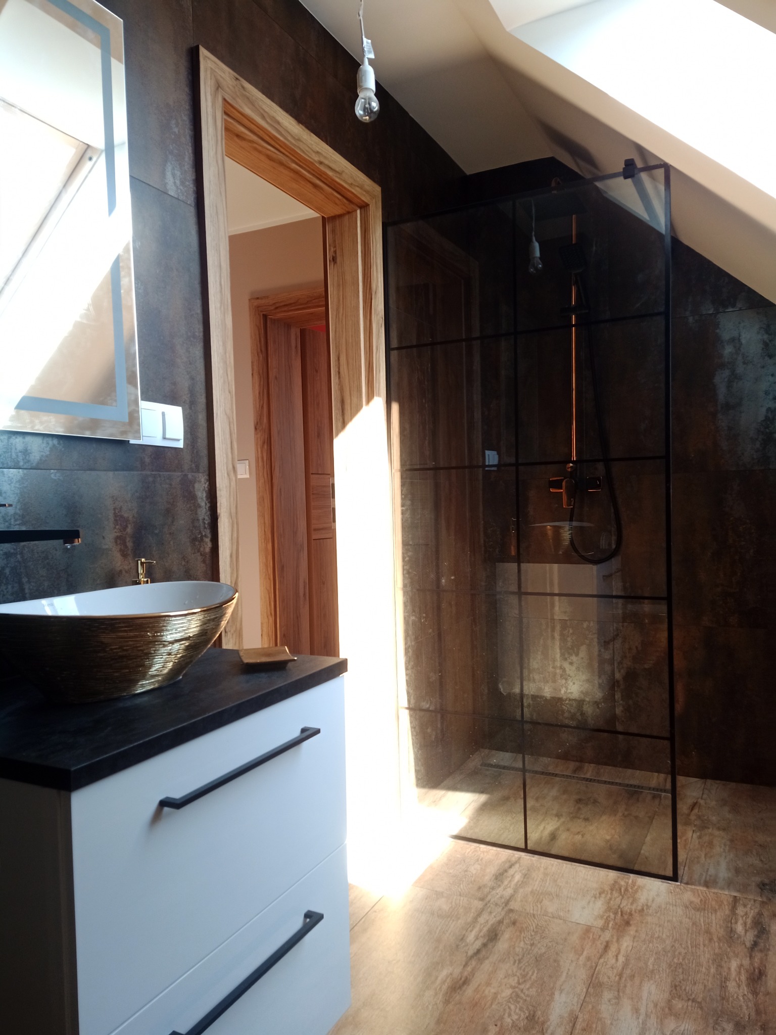 Nowoczesna łazienka na poddaszu z kabiną prysznicową typu walk-in, umywalką w kolorze złota i drewnianymi akcentami.