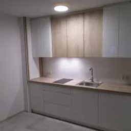 Nowoczesna kuchnia z białymi szafkami dolnymi i górnymi, oraz drewnopodobnymi szafkami górnymi, oświetlona lampą sufitową i listwą LED pod szafkami, z płytkami dekoracyjnymi na ścianie.